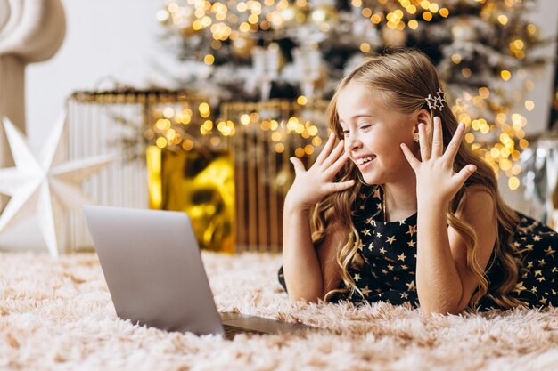 Foto piccola ragazza che usa il portatile e giace vicino all'albero di natale