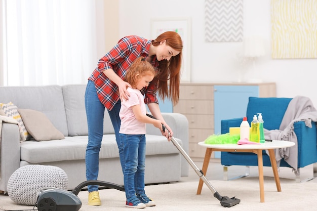 Little girl using vacuum cleaner while helping mother at home