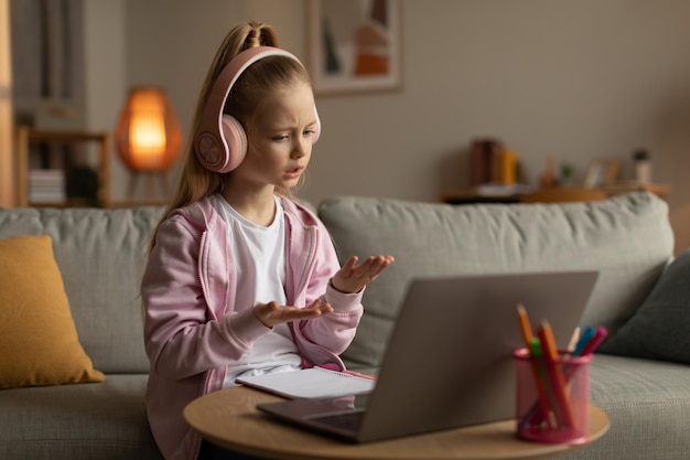 Фото Маленькая девочка по видеозвонку учится онлайн, разговаривая с ноутбуком в помещении