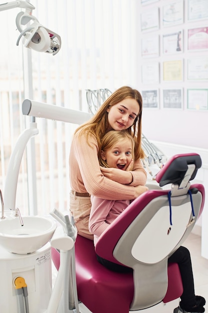 Маленькая девочка посещает стоматолога в клинике со своей мамой Концепция стоматологии