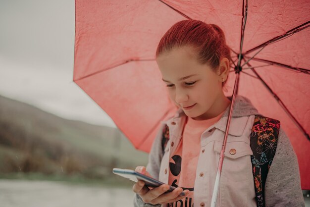 Little girl waiting for bus on rain day and using phone