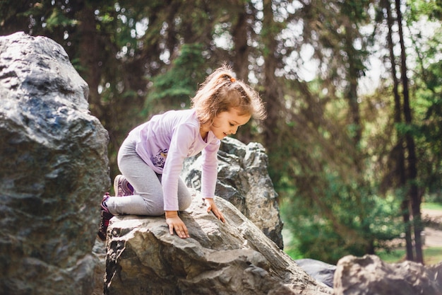 Bambina che cammina nel parco in estate, grandi rocce, arrampicata, escursionismo