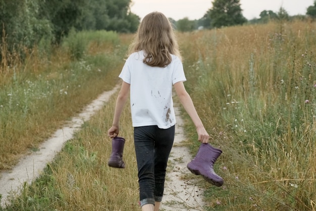 Little girl walking on rural road with rain boots in hands