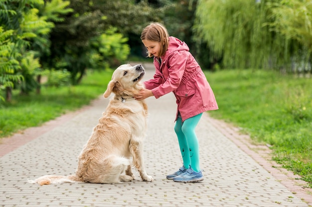 Little girl walking with golden retriever in green park