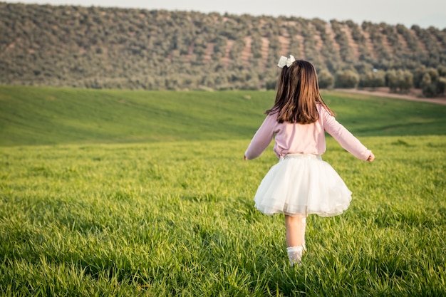 어린 소녀는 풀밭에 분홍색 셔츠와 치마와 함께 산책