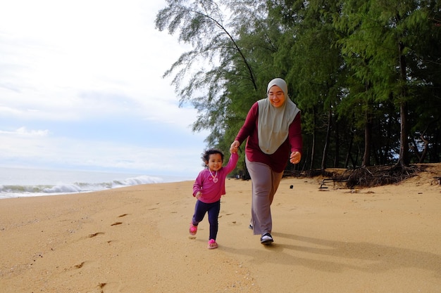 写真 小さな女の子が母親の手を握ってビーチの漂流木に沿って歩いています