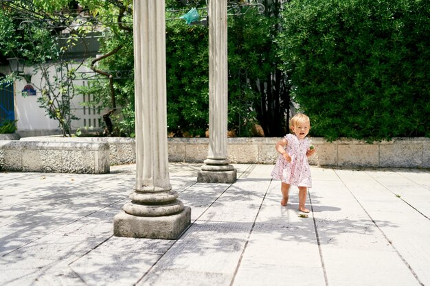 Little girl walks along a tiled path near the columns against the background of green magnolia