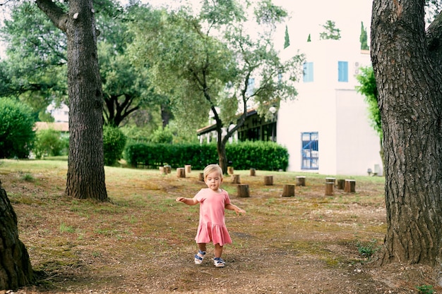 Little girl walks in a clearing near stumps in the courtyard of a house