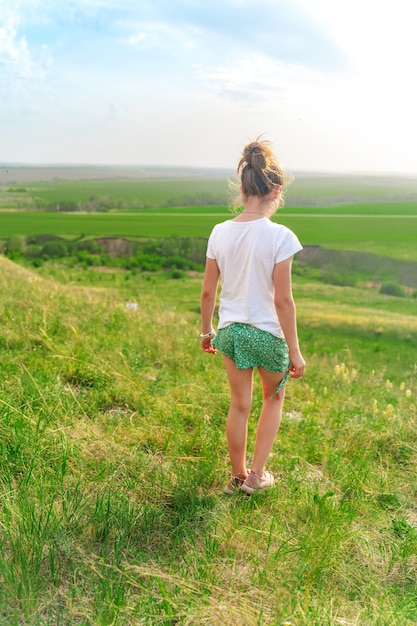 Little girl walks on a green meadow with a view of the hilly landscape