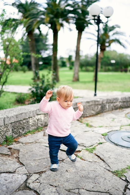 La bambina cammina sulle lastre per pavimentazione sullo sfondo degli alberi