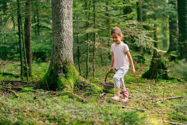 La bambina cammina attraverso la foresta con un cesto e raccoglie frutti di bosco e funghi