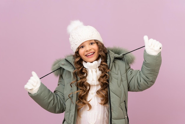 A little girl in a warm jacket and a knitted white hat with curly hair. a child in a warm winter jacket. cold season.