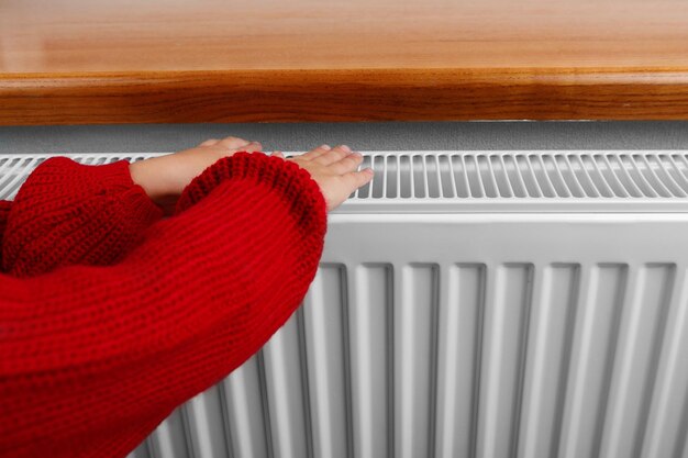 A little girl warms her hands and feet on a radiator