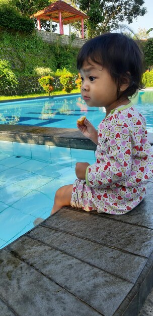 Little girl was daydreaming by the pool while holding a piece of snack person