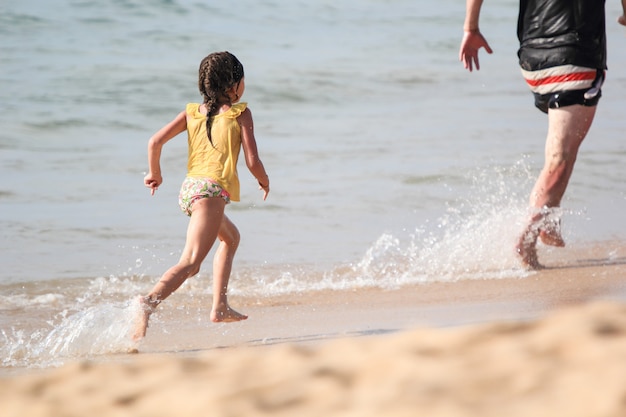 Photo little girl was playing chasing her father on the beach.