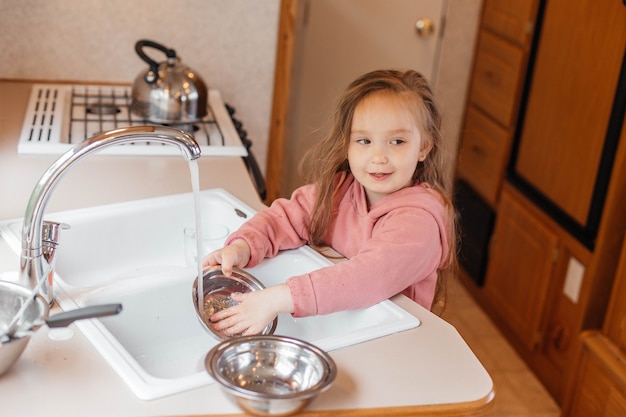 Bambina che lava i piatti nella cucina di una roulotte