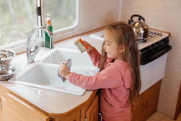 旅行トレーラーのキッチンで皿洗いをする少女