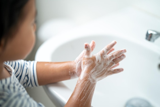 Маленькая девочка моет руки с мылом в раковине