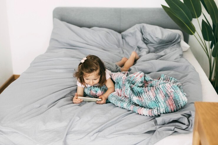 Photo a little girl watches cartoons on her phone or plays on the bed before going to bed top view