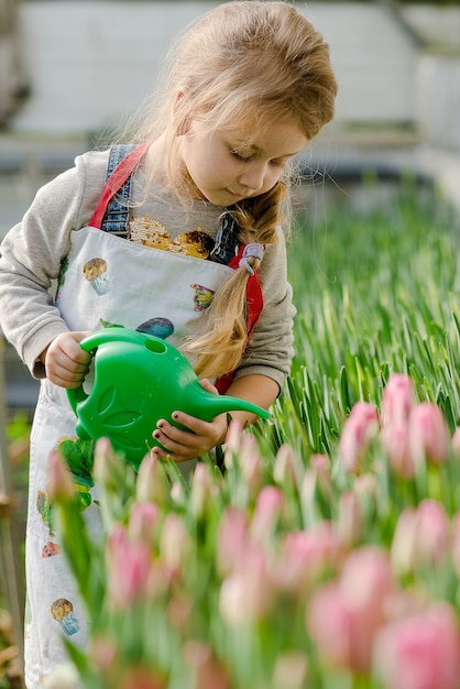 Little girl watering flowers in a greenhouse in spring.