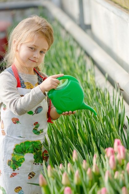 Little girl watering flowers in a greenhouse in spring.