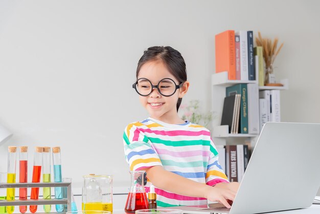 小さな女の子は、白い部屋で試験管科学実験に取り組む明るい色のシャツを着ています