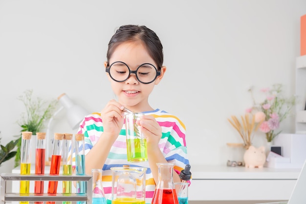 маленькая девочка в яркой рубашке работает с научным экспериментом в пробирке в белой комнате