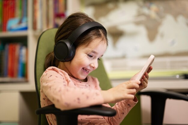 Little girl wear headphones watching cartoons or kid video on her phone