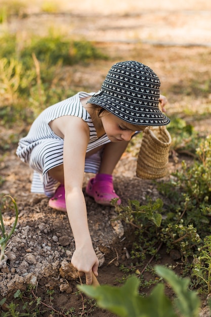 写真 野菜の庭でうずくまる帽子をかぶっている少女