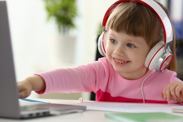 Little girl wearing headphones use mobile computer