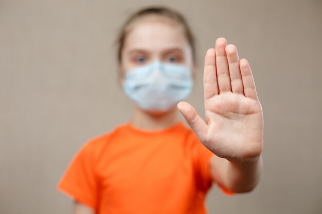 保護のためのマスクを身に着けている女の子。一時停止の標識を表示しています。ウイルスと流行病を阻止する。コロナウイルスcovid-19.stay at home stay safe concept。手にセレクティブフォーカス。
