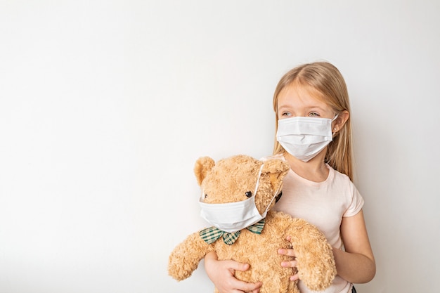 Little girl wearing mask and holding her teddy bear