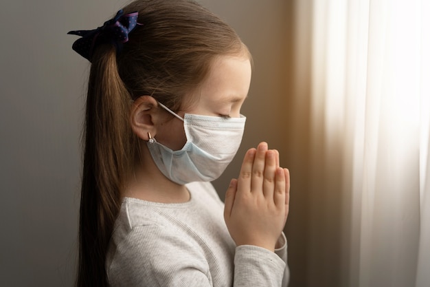 Little girl wearing mask for protect Covid-19. She praying in the morning for a new day freedom to world corona virus. Little girl hand praying for thank GOD