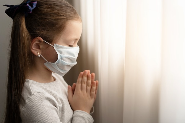 Little girl wearing mask for protect Covid-19. She praying in the morning for a new day freedom to world corona virus. Little girl hand praying for thank GOD.