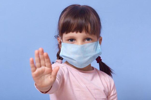 Little girl wearing medical face mask and making stop sign with her palm