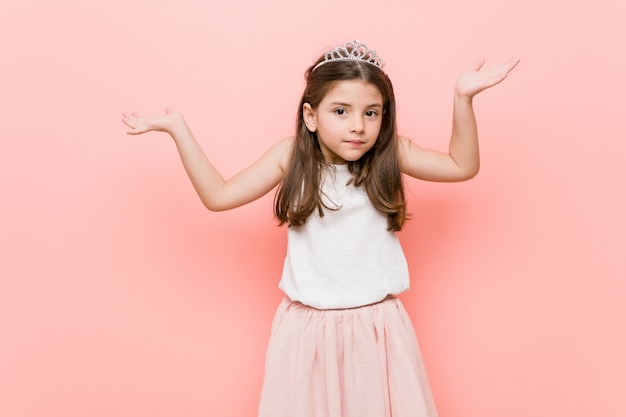 Little girl wearing a princess look doubting and shrugging shoulders in questioning gesture.