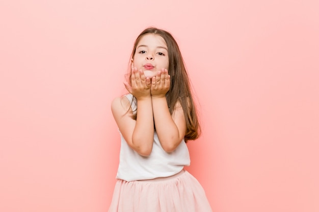 Little girl wearing a princess look folding lips and holding palms to send air kiss