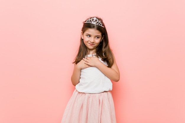 Little girl wearing a princess look has friendly expression, pressing palm to chest