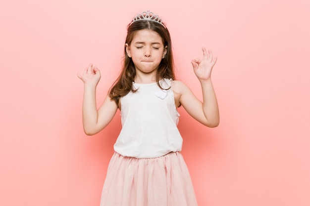 Little girl wearing a princess look relaxes after hard working day, she is performing yoga.