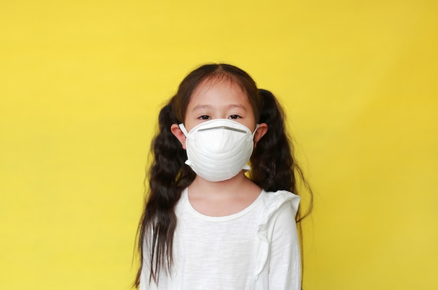 노란색 배경에 대기 오염에 대한 보호 마스크를 착용하는 어린 소녀