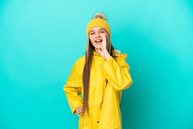 Little girl wearing a rainproof coat over isolated blue background shouting with mouth wide open