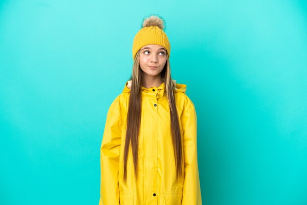 孤立した青い壁に防雨コートを着て見上げる少女