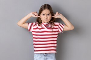 Фото Маленькая девочка в полосатой футболке, закрывающей уши, чтобы не слушать советы, игнорируя воспитание и воспитание