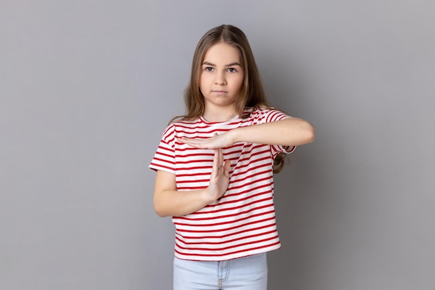 Little girl wearing Tshirt showing time out gesture looking at camera deadline with test in school