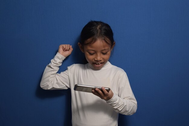 Little girl wearing white tshirt playing game on smart phone with surprised face and clenching fits