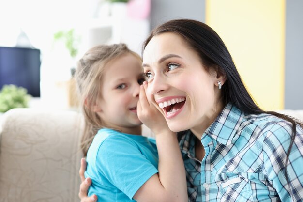 Little girl whispering secret to mom ear at home