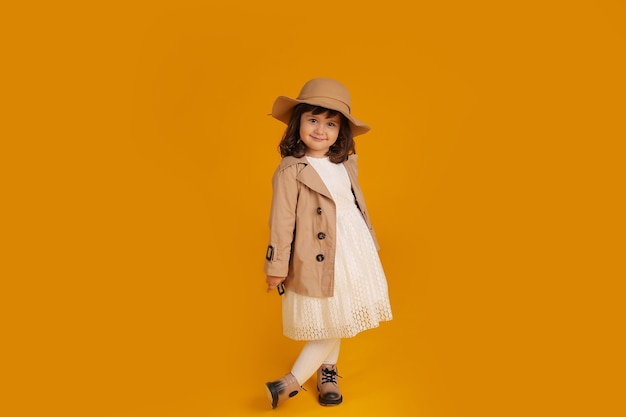 Little girl white dress beige raincoat beige hat beige boots yellow background