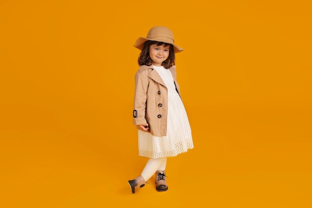 little girl white dress beige raincoat beige hat beige boots yellow background