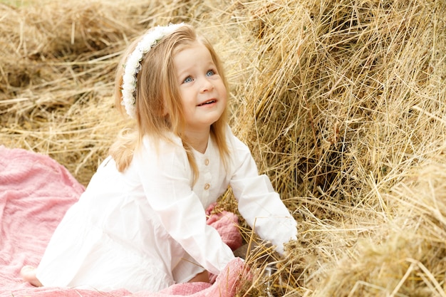 Little girl in a white dress on the hay in nature