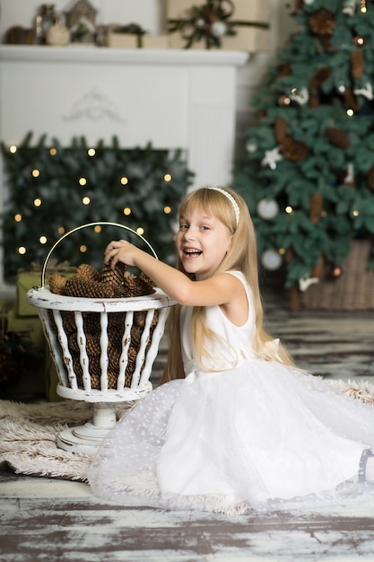 Little girl in a white dress plays with pine cones in Christmas decorations